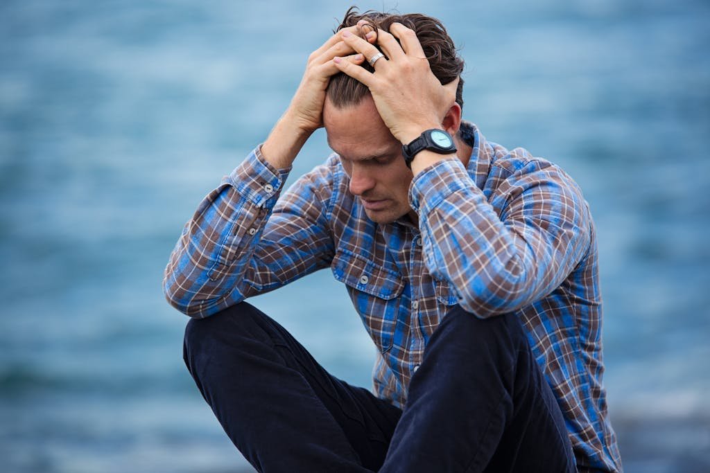 A man in a plaid shirt sits by the water processing his grief