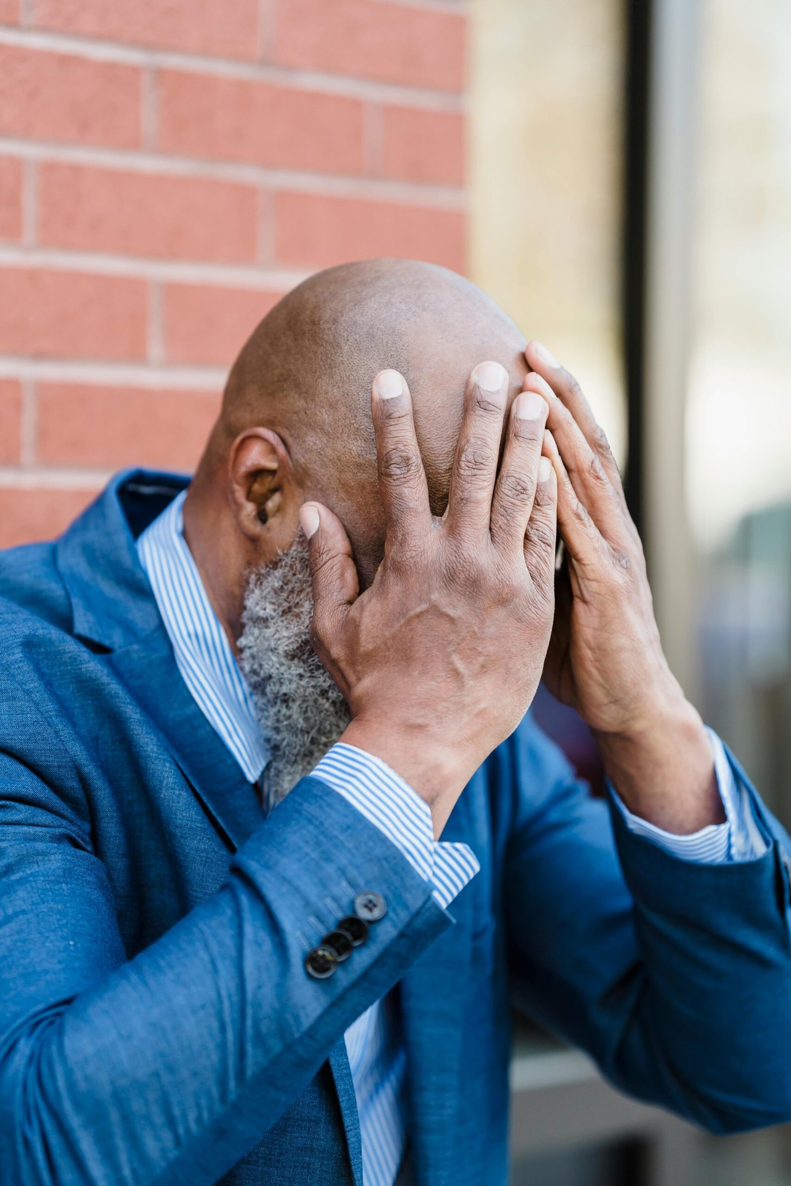 Man in a blue suit holds his hands to his face after losing his job