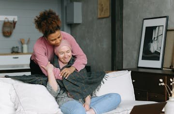 Two women share a caring embrace in a cozy, modern living room, embodying support for a terminally ill cancer sufferer