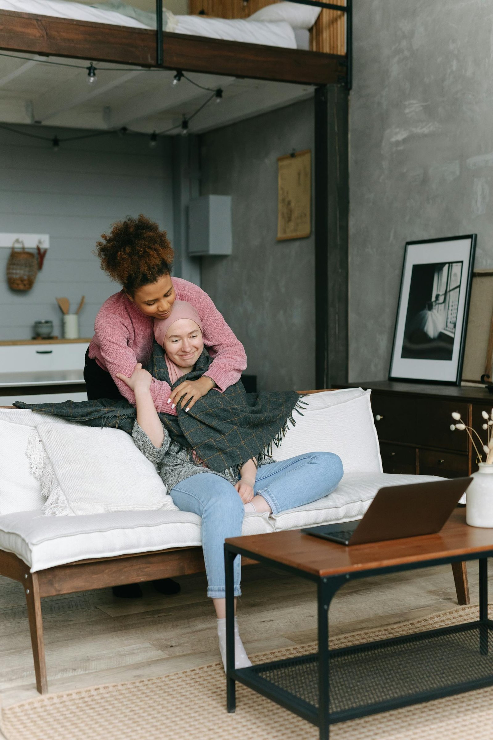 Two women share a caring embrace in a cozy, modern living room, embodying support for a terminally ill cancer sufferer