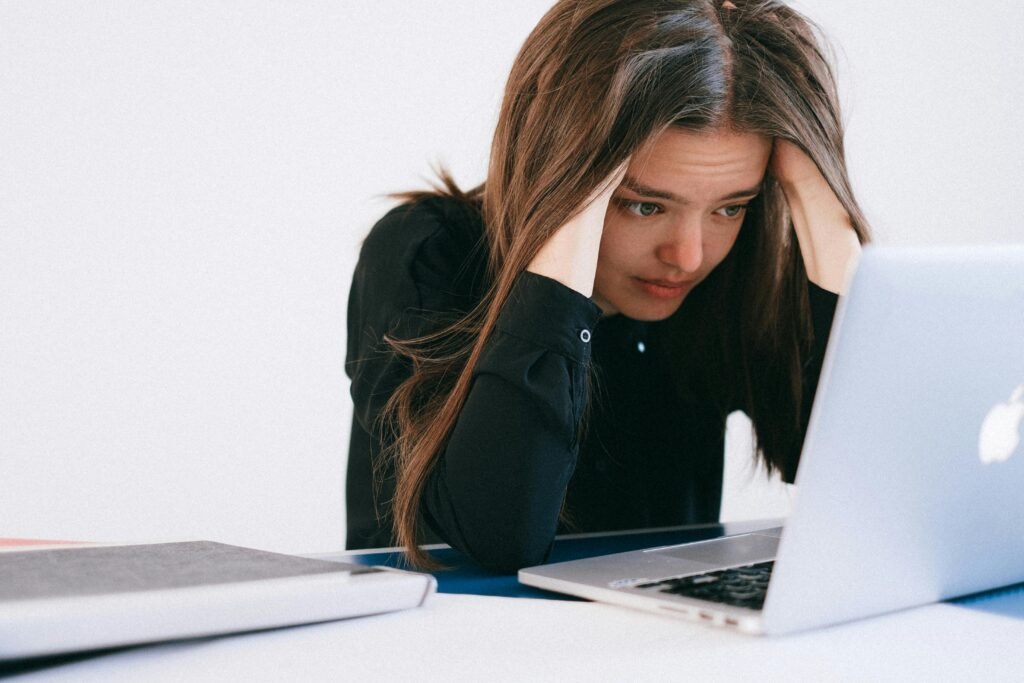 Woman sitting in front of a laptop, holding her head in her hands feeling overwhelmed by responsibility