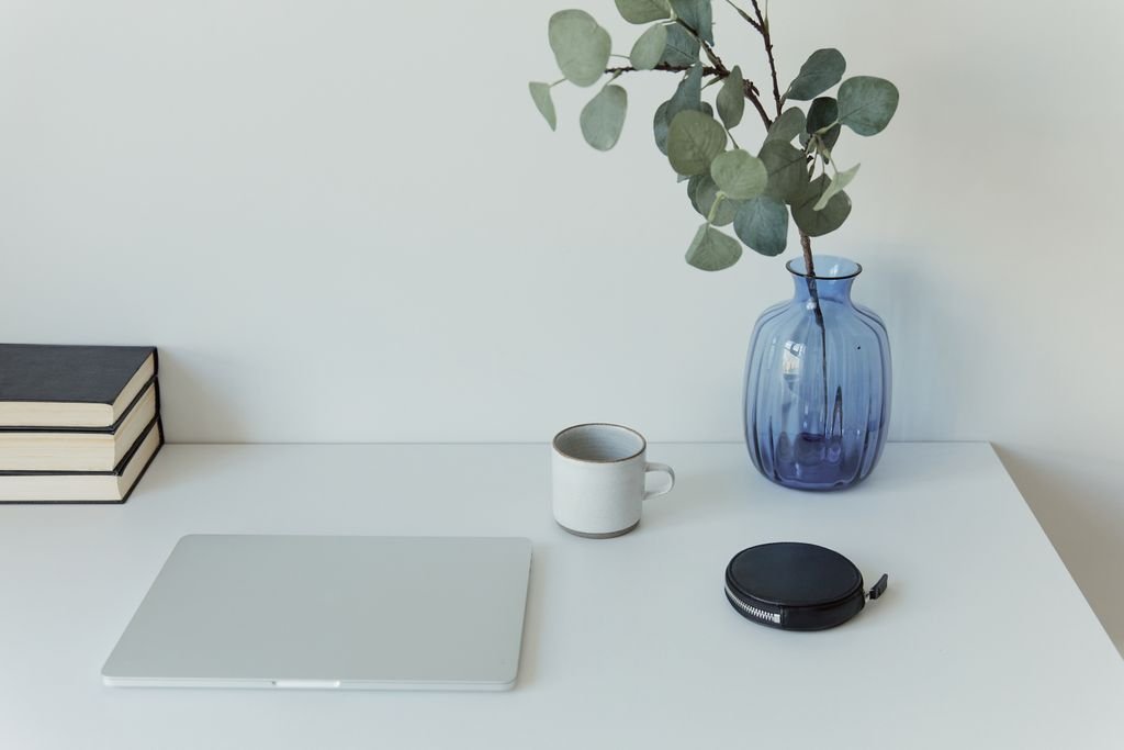 White desk with a laptop, blue vase with plant, and coffee mug, set up for online counselling at The Beach Haven.