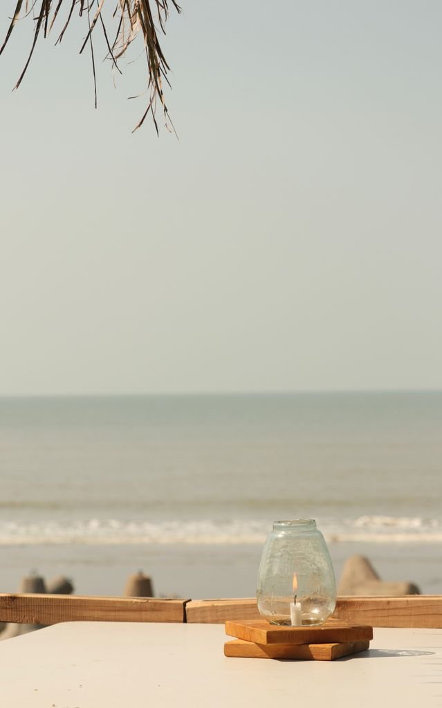 Peaceful ocean view with a candle in a glass shade on a wooden table.