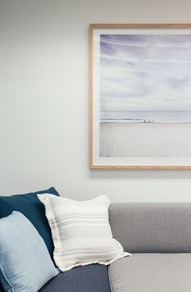 Soft couch with pillows in The Beach Haven's counselling rooms in clarkson, decorated with framed picture of beach and sea hanging on white wall