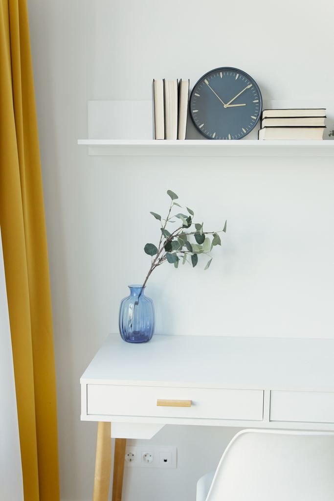 Stylish workspace featuring a blue vase with eucalyptus, books, and a clock on a white table in a counselling room at the Beach Haven used for personal growth counselling
