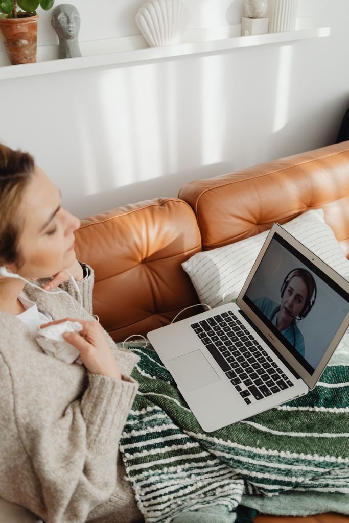 Woman wearing earphones having an online counselling session on a laptop, sitting comfortably in a cozy home setting.
